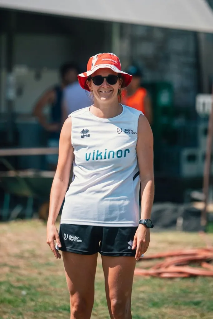 Emilie smiling in a Rugby Danmark kit and a red bucket hat at a tournament